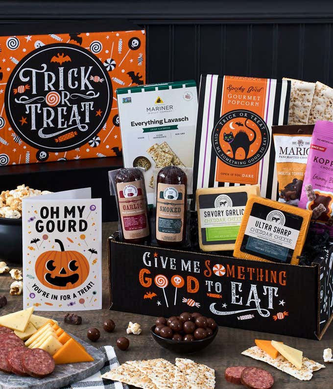 A Halloween-themed gift box featuring a variety of snacks, including cheddar cheese, summer sausage, crackers, gourmet popcorn, black and white cookies, gummy bears, and chocolate-covered treats, with a 