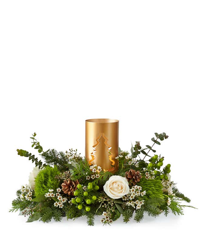Holiday centerpiece featuring white roses, green button poms, pinecones, berries, and evergreen branches arranged around a gold metal candle holder with a cut-out Christmas tree design.