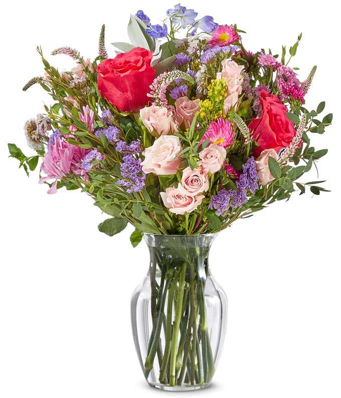 a bright bouquet of peach mini roses, hot pink full sized roses, light pink and bright pink matsumoto asters, greenery, and dark blue delphinium flowers arranged as a bouquet.