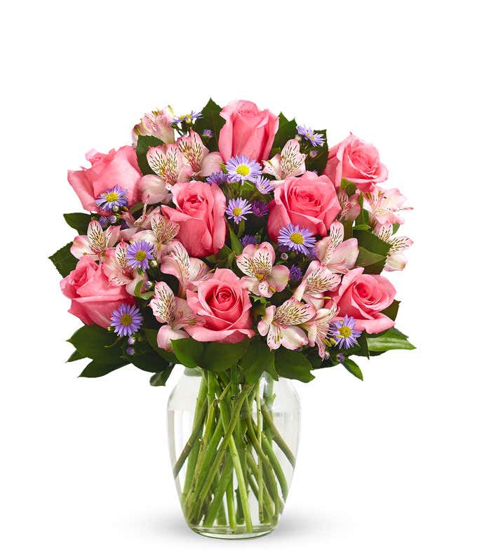 A bouquet of pink roses, white alstroemeria, and lavender aster in a glass vase 