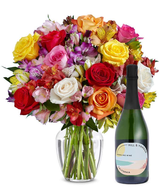 A mix bouquet of roses and alstroemeria fills a clear glass vase and is paired with a bottle of Hill & Harbor California Pinot Noir.
