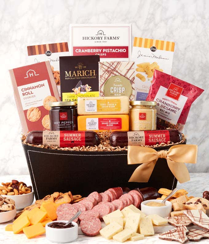 A  black gift basket with two packs of sausage, a wheel of gouda cheese, a block of cheddar cheese, a jar of honey pineapple mustard, a jar of hot & sweet mustard, and fig chutney, a box of chocolate chip mini biscotti, chocolate chip cookies, toffee pret