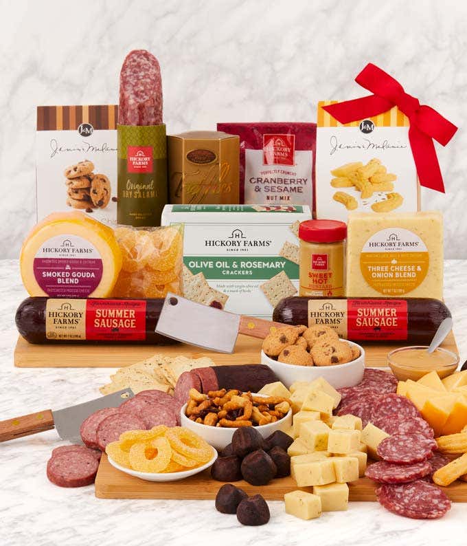 Charcuterie gift set with Hickory Farms summer sausages, smoked Gouda and three cheese & onion cheeses, crackers, cookies, nut mix, dried fruit, mixed nuts, and chocolate-covered pretzels, arranged on a wooden board with cheese knives.