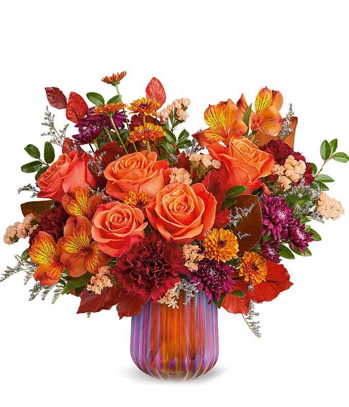 Orange Roses, Orange Alstroemeria, Burgundy Carnations, Bronze Poms, Purple Poms, and floral greenery in a sage green pitcher