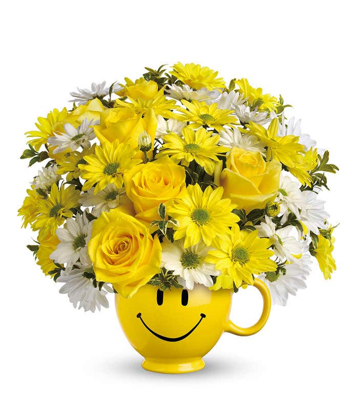 Yellow roses and bright daisies in a yellow smiley face mug