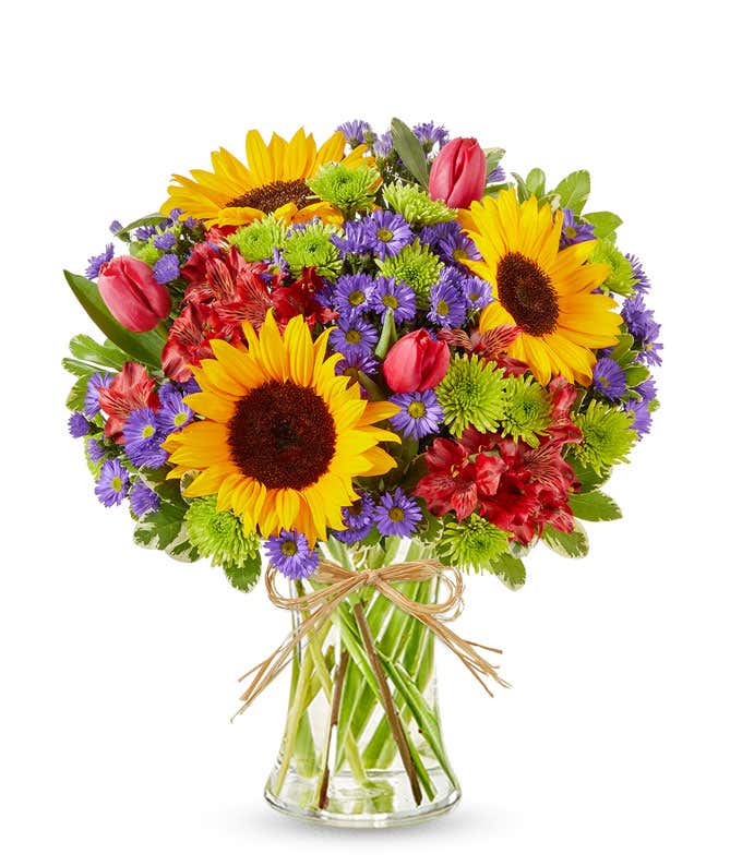 Sunflowers and pastel flowers in a clear glass vase with raffia tie