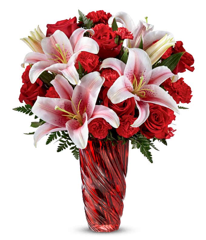 Red roses, red carnations, and pink lilies in a red swirled vase