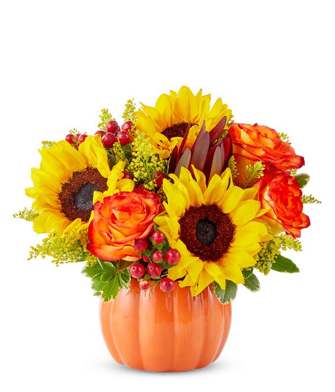 sunflowers, orange roses, red hypericum berries, yellow solidago, and greenery arranged in a glossy orange pumpkin-shaped vase