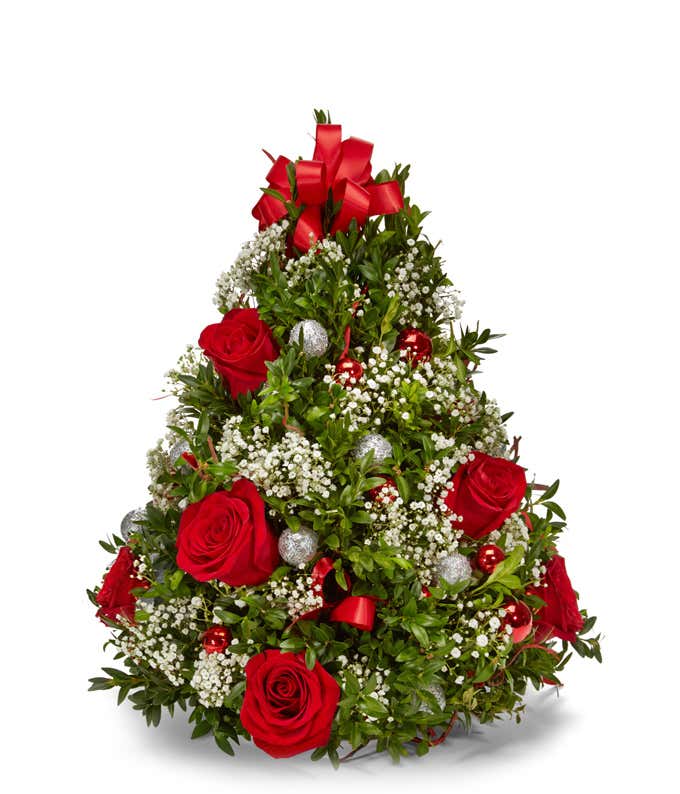 Christmas tree-shaped floral arrangement featuring red roses, baby's breath, lush greenery, silver and red ornament balls, and a large red bow on top.