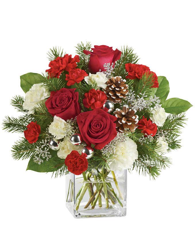 A festive arrangement with red roses (deluxe & premium only), red carnations, white carnations, red mini-carnations, white mini-carnations, seasonal greens, silver ornaments, and pine cones.