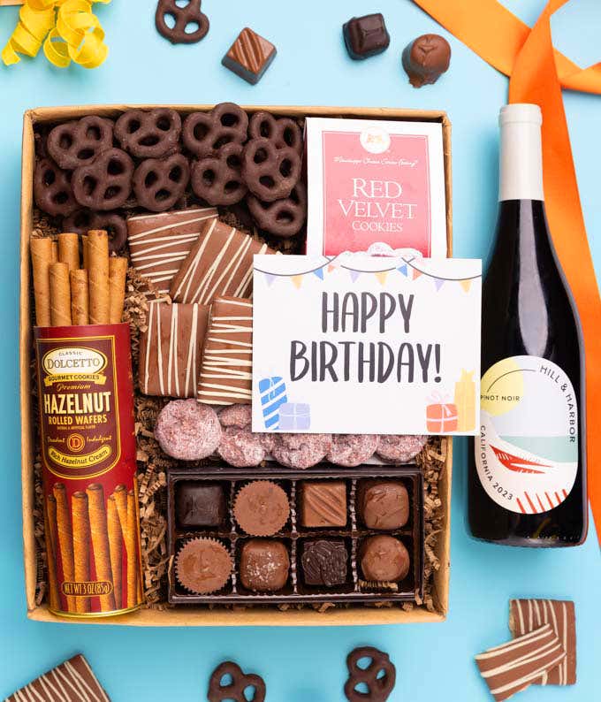 a gift box full of decadent treats with a Birthday message card.  Contents include: a bottle of California Pinot Noir, a bag of milk chocolate pretzel, a box of mini chocolate chip cookies, and a 4-ounce box of assorted chocolates.