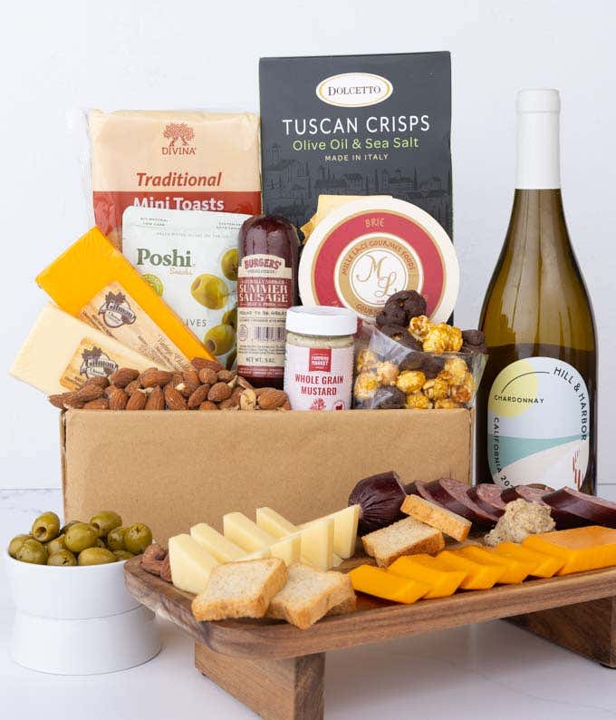 A charcuterie gift set with Tuscan crisps, focaccia crackers, 3 cheeses, olives, mustard, sausage almonds, chocolate-covered popcorn and a bottle of California Chardonnay.