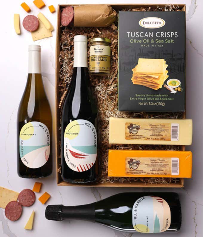 A gift box with three bottles of California wine (red, white, and sparkling), two types of cheese, crackers, stone-ground mustard, and a summer sausage.