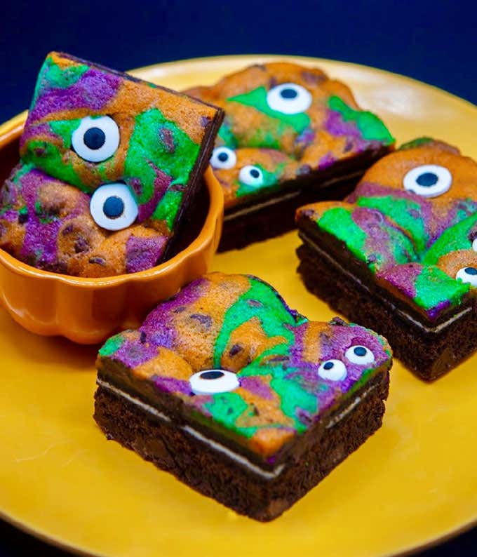 Four monster brookie squares on a plate with orange, purple, and green swirl patterns and eye sprinkles