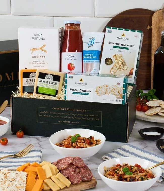 Gift ox with a box of grilled crostini toasta, jar of pasta sauce, blocks of garlic and vegetable cheese, sweet Soppressata, and chocoate bites. In front of the box is a grazing tray with crostini toasts, sliced Soppressata, cubed cheese, water crackers, 