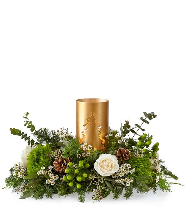 Holiday centerpiece featuring white roses, green button poms, pinecones, berries, and evergreen branches arranged around a gold metal candle holder with a cut-out Christmas tree design.