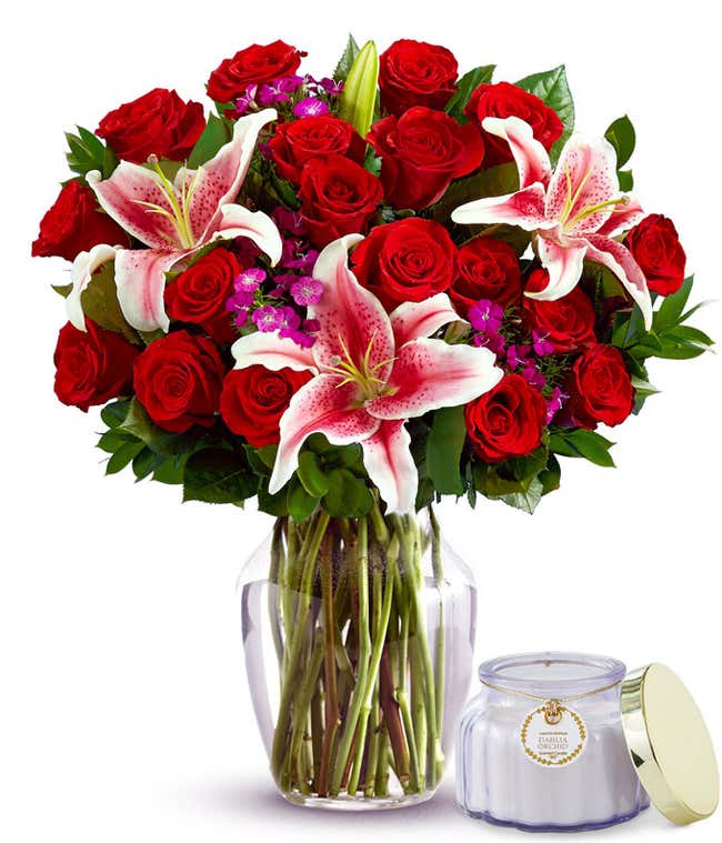 18 red roses, Stargazer lilies, pink dianthus, floral greens, optional glass vase sitting next to a small purple candle