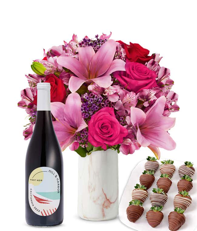A mixed bouquet of pink and purple flowers in a clear glass vase is displayed with a bottle Hill &amp; Harbor Pinot Noir and 12 chocolate-covered strawberries.