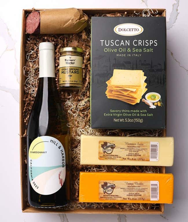 A gift box with a bottle of California Chardonnay, two types of cheese, crackers, stone-ground mustard, and a summer sausage.