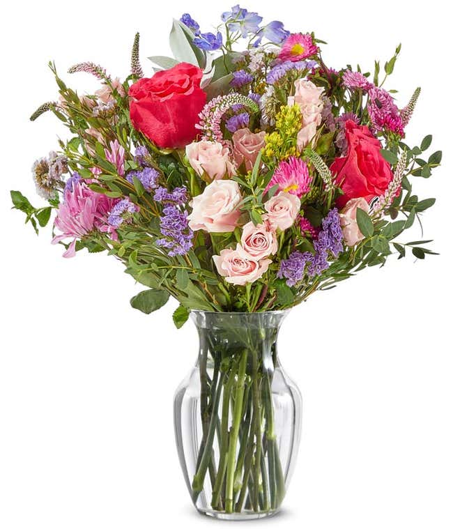 a bright bouquet of peach mini roses, hot pink full sized roses, light pink and bright pink matsumoto asters, greenery, and dark blue delphinium flowers arranged as a bouquet.