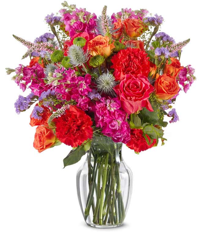 A hand-tied bouquet of hot pink roses, red blooms, purple flowers, thistle accents, green filler, and leafy greenery in a fresh and colorful garden-inspired style.