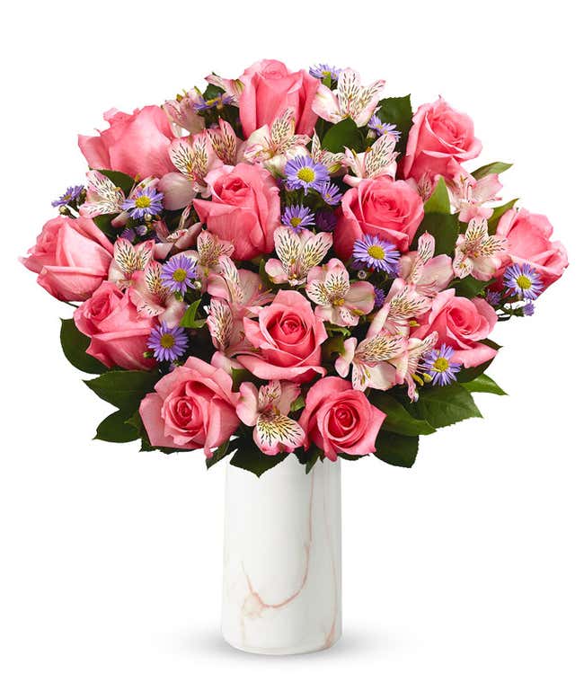 A bouquet of pink roses, white alstroemeria, and lavender aster in a glass vase 