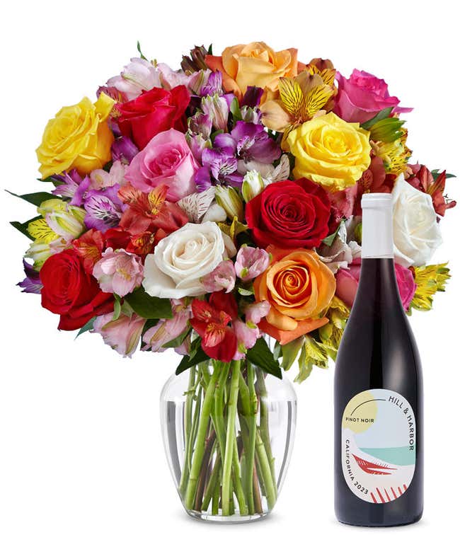 A mix bouquet of roses and alstroemeria fills a clear glass vase and is paired with a bottle of Hill &amp; Harbor California Pinot Noir.