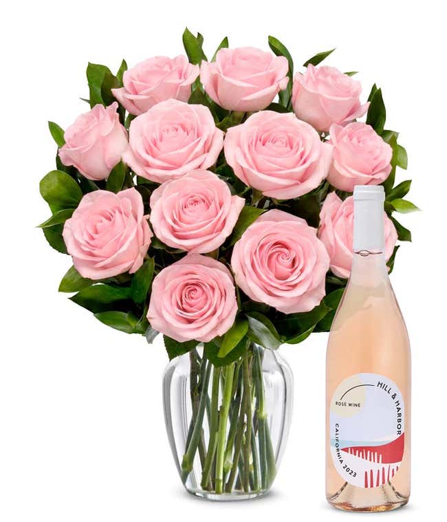 A bouquet of 12 soft pink roses arranged in a clear glass vase is displayed next to a bottle of Hill &amp; Harbor California Ros&eacute;.