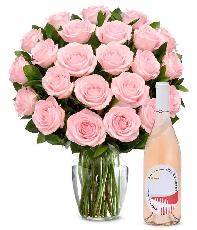 A bouquet of 24 soft pink roses arranged in a clear glass vase is displayed next to a bottle of Hill &amp; Harbor California Ros&eacute;.