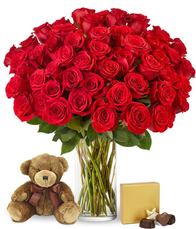 Image of 50 long-stemmed red roses in a tall cylinder vase, accompanied by a box of chocolates and a cuddly teddy bear, the perfect gift for expressing love and affection.