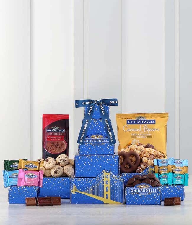 Ghirardelli-themed gift tower with blue boxes featuring golden bridge designs. Contains an assortment of Ghirardelli chocolates, including squares, minis, hot cocoa mix, caramel popcorn, cookies, and chocolate-covered almonds, tied with a Ghirardelli ribb