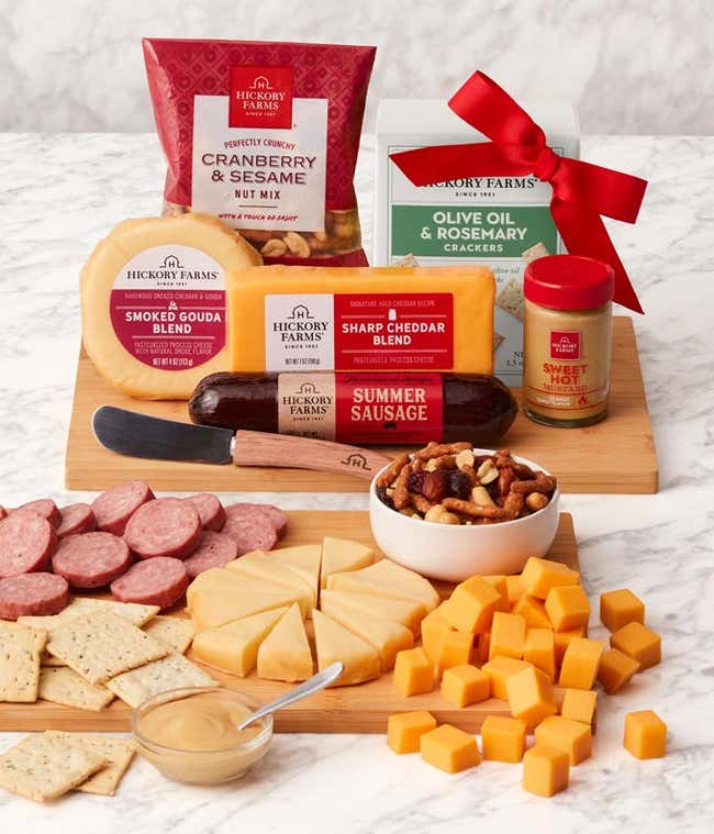 Gourmet gift set with Sharp Cheddar, Smoked Gouda, Olive Oil &amp; Rosemary Crackers, Cranberry &amp; Sesame Nut Mix, Farmhouse Summer Sausage, and Sweet Hot Mustard, displayed on a bamboo cutting board with a cheese spreader.