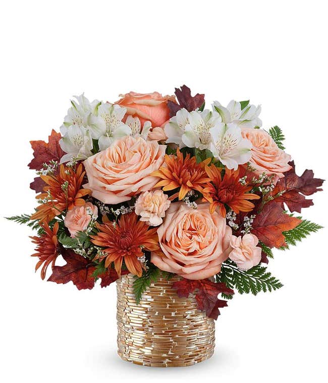Fall floral arrangement with peach roses, white alstroemeria, bronze cushion spray chrysanthemums, peach miniature carnations, and autumn leaves in a gold-glass textured vase.