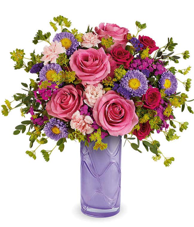 Pink Roses, Hot Pink Spray Roses, Mini Pink Carnations, Dark Pink Sweet William, Lavender Asters, and floral greenery in a purple glass cylinder vase