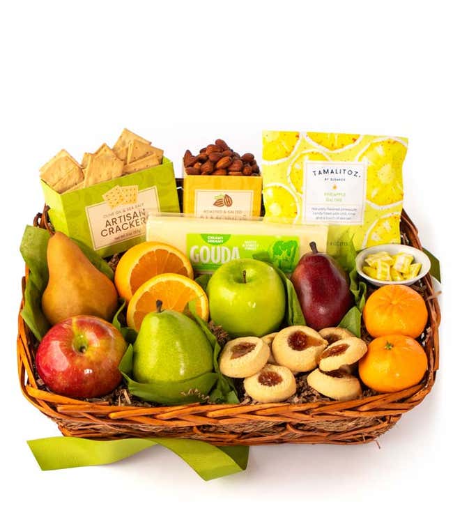 A basket filled with fresh fruits, crackers, cheese crisps, almonds, honey mustard, and assorted caramels, adorned with a green ribbon. 