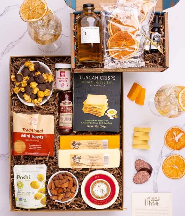 The food box contains three cheeses, summer sausage, crackers, olives, almonds, popcorn and mustard.  The cocktail box contains thyme-cucumber syrup, celery bitters, grapefruit oil mist, dehydrated grapefruit slices, and recipe card.