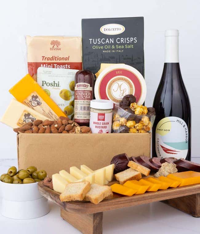 A charcuterie gift set with Tuscan crisps, focaccia crackers, 3 cheeses, olives, mustard, sausage almonds, chocolate-covered popcorn and a bottle of Pinot Noir.