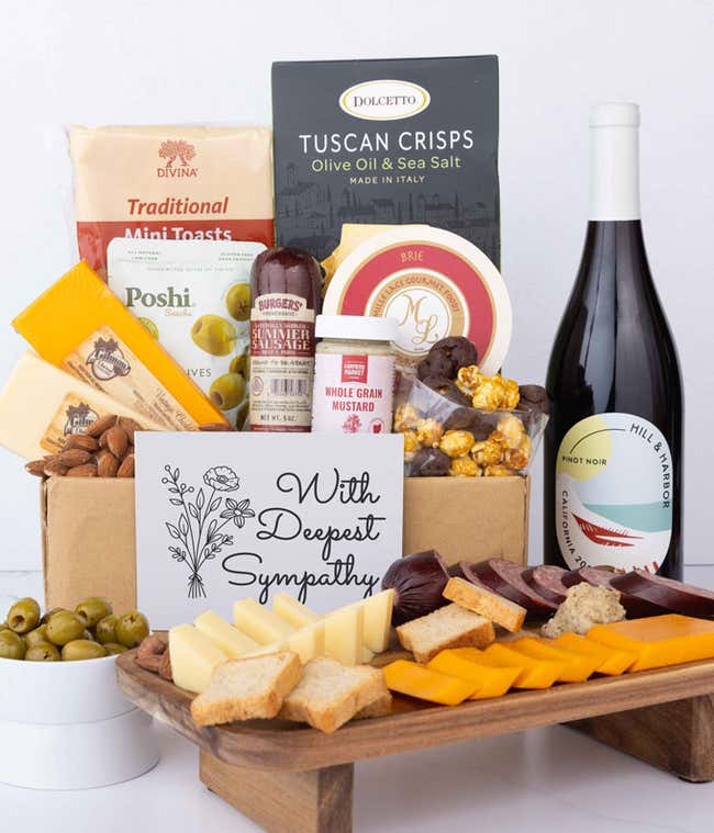 An abundent charcuterie gift set with Tuscan crisps, focaccia crackers, 3 cheeses, olives, mustard, summer sausag, almonds, chocolate-covered popcorn, a bottle of Pinot Noir, and a sympathy card. 