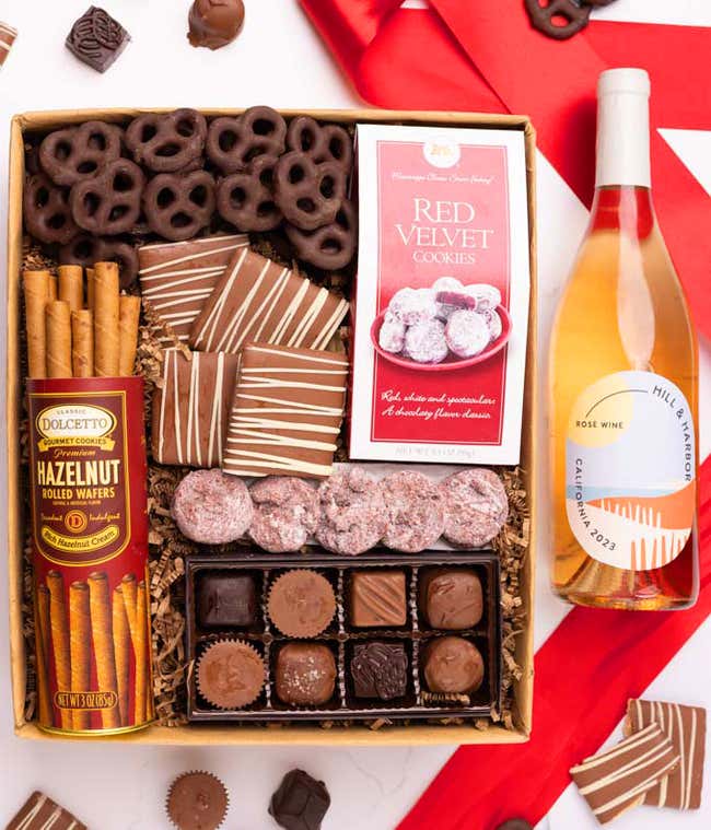 A gift box with chocolate pretzels, chocolate graham crackers, red velvet cookies, hazelnut wafer rolls, an 8 piece box of chocolates and a bottle of ros&eacute; wine.