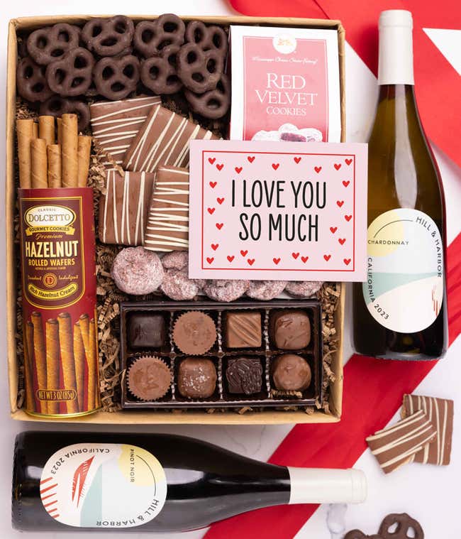 A gift box with chocolate pretzels, chocolate graham crackers, red velvet cookies, hazelnut wafer rolls, an 8 piece box of chocolates, 2 bottles of wine and an I Love You message card.