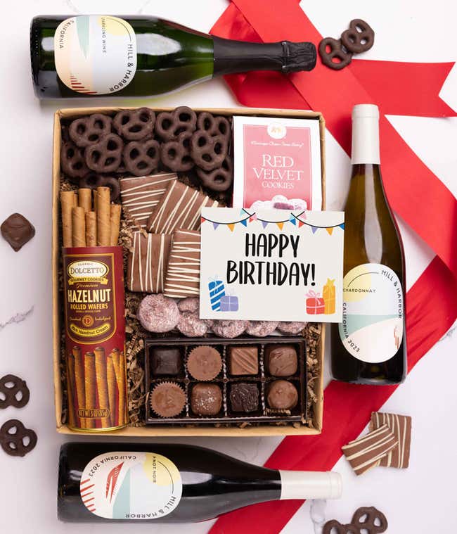 A gift box with chocolate pretzels, chocolate graham crackers, red velvet cookies, hazelnut wafer rolls, an 8 piece box of chocolates, 3 bottles of wine and a Birthday message card.