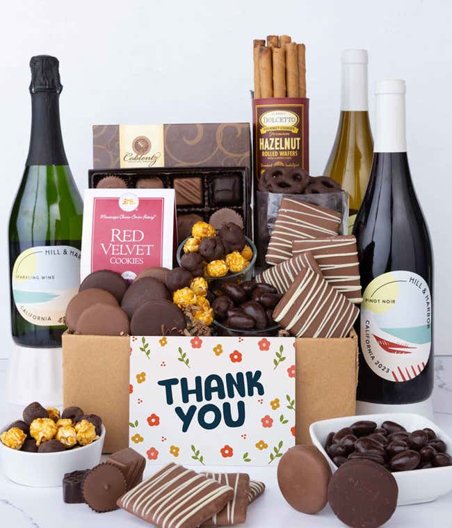 A gift box overflowing with treats including an assortment of chocolate-covered items like oreoes, almonds graham crackers and pretzels along with red velvet cookies, hazelnut wafers, an 8 piece box of chocolates, 3 bottles of wine and a Thank You card.